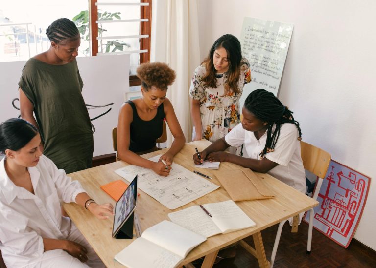 Une équipe diversifiée collabore à un projet en utilisant des ressources numériques et papier dans un bureau lumineux.